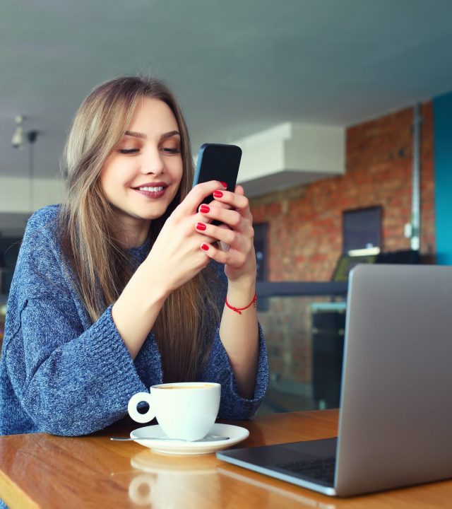 Woman typing text message on smart phone in a cafe. Young woman sitting at a table with a coffee using mobile phone. With blank copy space scree for your advertising text message or promotional content Toned image. Selective focus.